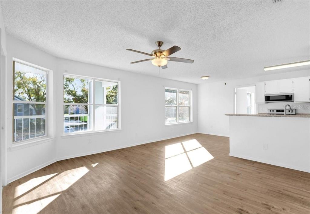 An open-concept living area with light wood-look flooring, white walls, and a ceiling fan — 2585 GRASSY POINT DRIVE UNIT 211, LAKE MARY, FL