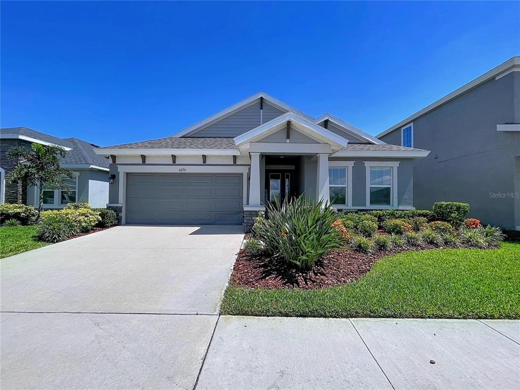 A single-story suburban house features a gray garage, a covered entryway, and landscaped front yard — 6290 ROADSTEAD COURT, APOLLO BEACH, FL