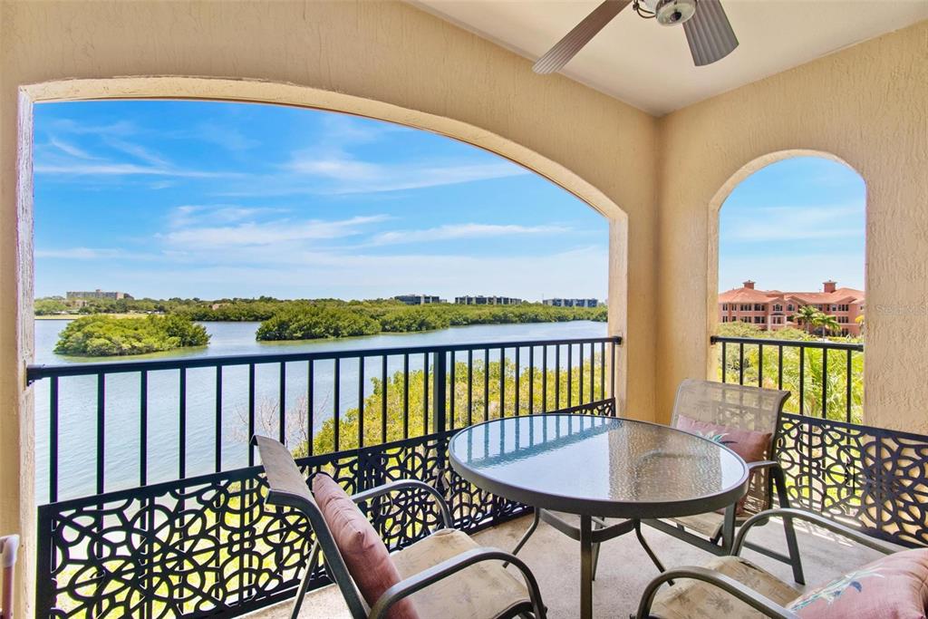 A covered balcony features a glass-topped table, chairs, and a view of water and mangroves — 2739 VIA CAPRI UNIT 1039, CLEARWATER, FL