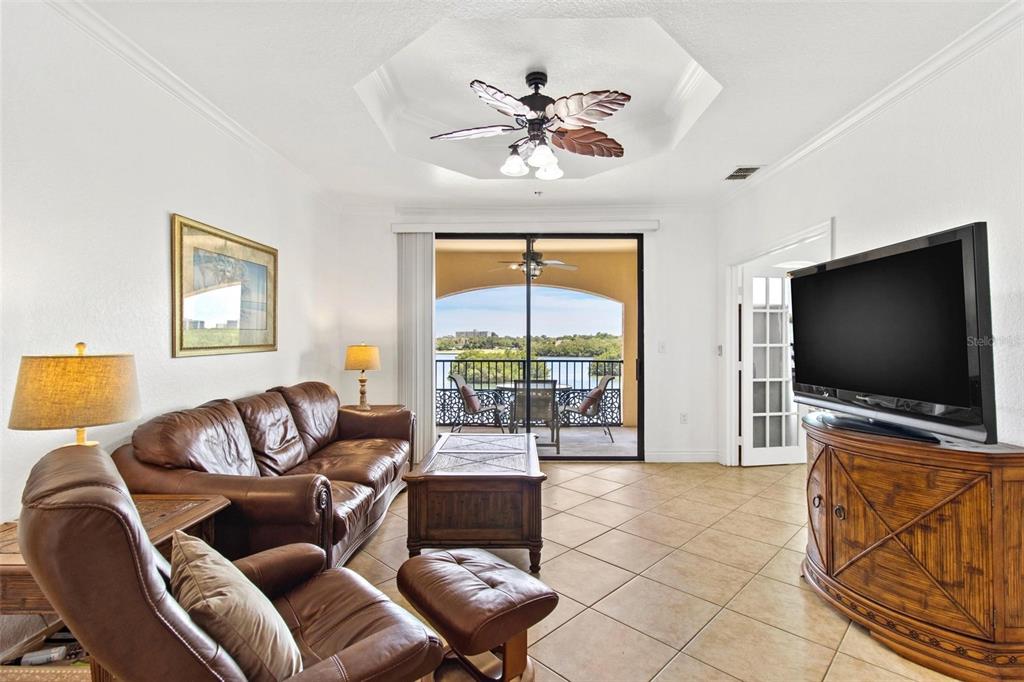 A living room features leather furniture, a tray ceiling with a fan, and a balcony view — 2739 VIA CAPRI UNIT 1039, CLEARWATER, FL