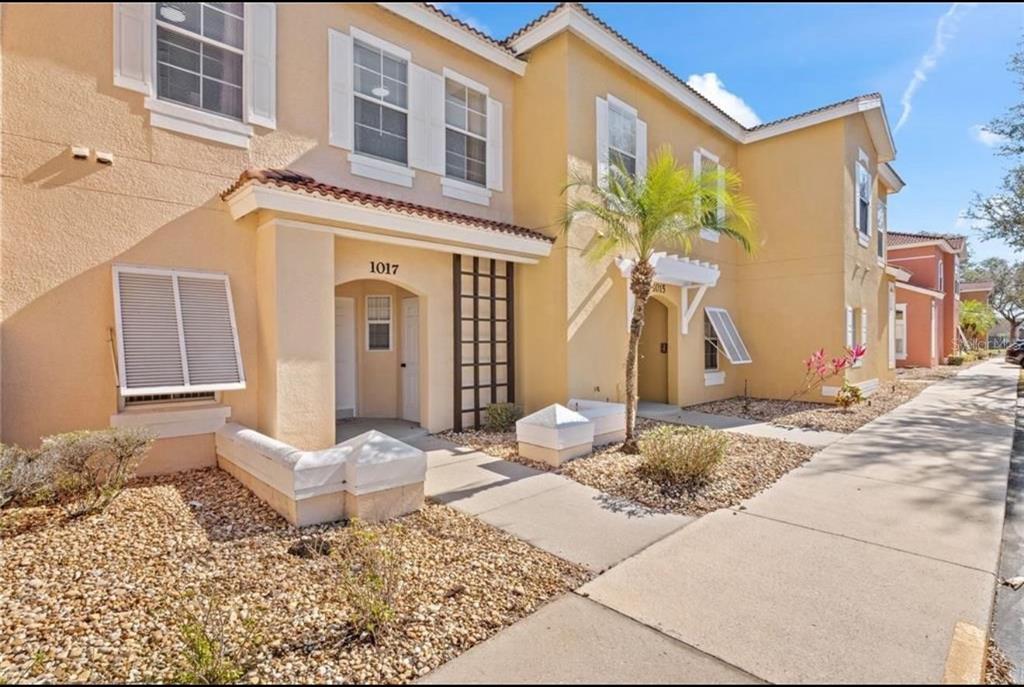 A two-story tan stucco townhouse exterior with a palm tree and a concrete walkway — 1017 PARK RIDGE CIRCLE, KISSIMMEE, FL