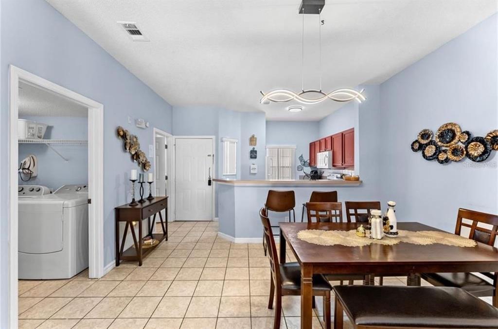 A dining area with tile floors, a wooden table, and an open kitchen with red cabinets — 1017 PARK RIDGE CIRCLE, KISSIMMEE, FL