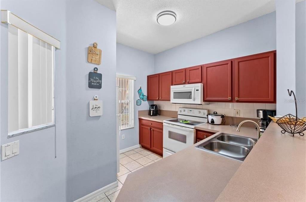 A kitchen features red cabinets, white appliances, a double sink, and light-colored countertops — 1017 PARK RIDGE CIRCLE, KISSIMMEE, FL