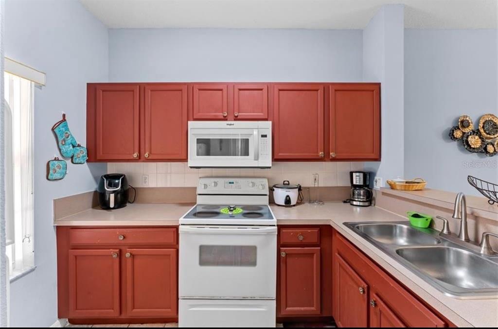 A kitchen with red cabinets, white appliances, a double sink, and light-colored countertops — 1017 PARK RIDGE CIRCLE, KISSIMMEE, FL