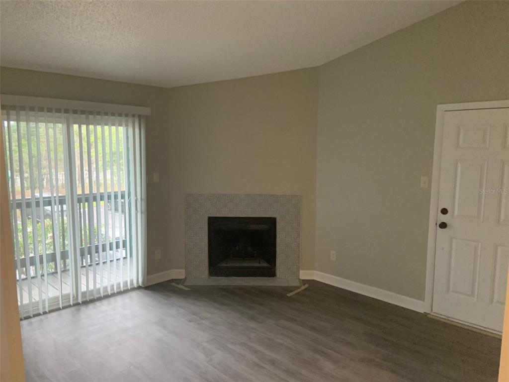 A living room features gray wood-look flooring, a tiled fireplace, and a sliding glass door — 3756 IDLEBROOK CIRCLE UNIT 204, CASSELBERRY, FL
