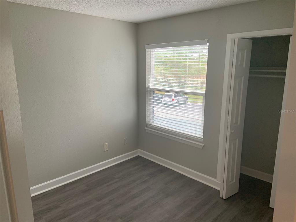 A small bedroom with gray walls, wood-look flooring, a window with blinds, and a closet — 3756 IDLEBROOK CIRCLE UNIT 204, CASSELBERRY, FL