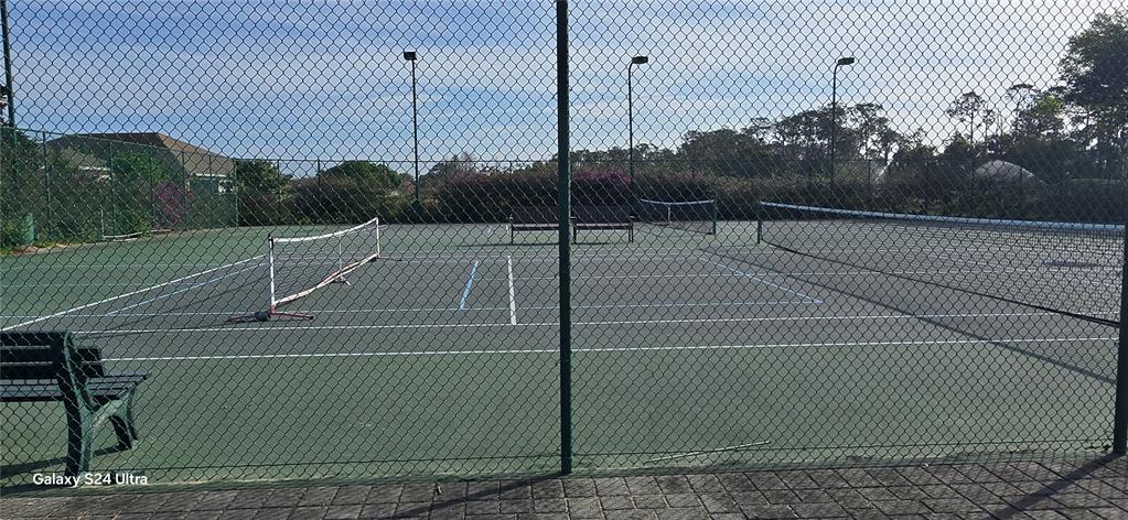 A fenced outdoor tennis court features a net, benches, and overhead lighting poles — 18410 BLUE HERON CIRCLE, DEER ISLAND, FL