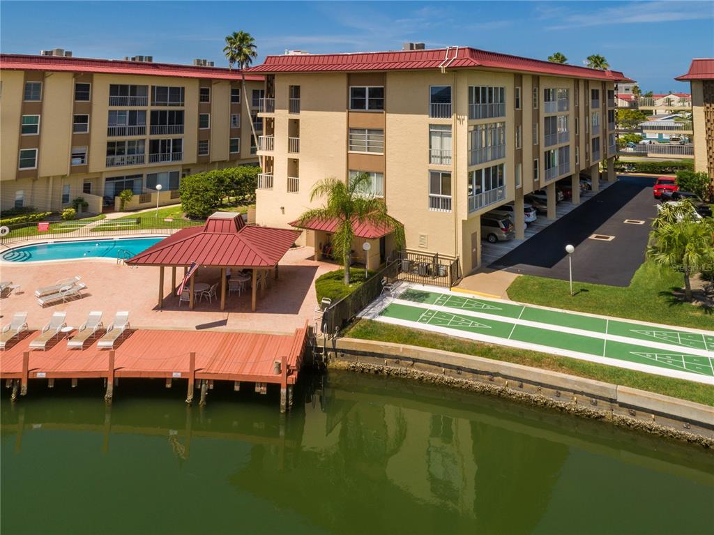 An aerial view of a waterfront apartment complex with a pool, deck, and shuffleboard court — 121 ISLAND WAY UNIT 334, CLEARWATER BEACH, FL