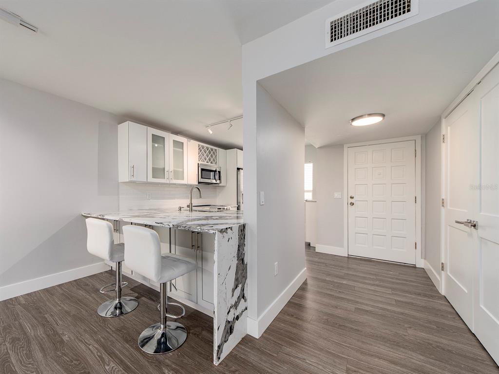 A kitchen with a marble waterfall island and two bar stools next to an entryway — 121 ISLAND WAY UNIT 334, CLEARWATER BEACH, FL