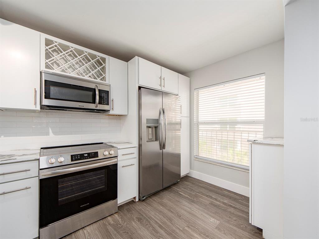 A kitchen with white cabinets, stainless steel appliances, and wood-look flooring next to a window — 121 ISLAND WAY UNIT 334, CLEARWATER BEACH, FL