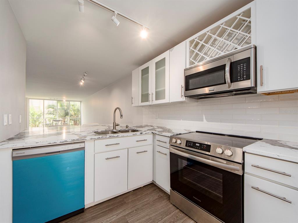 A kitchen features white cabinets, marble-look countertops, stainless steel appliances, and a bright blue dishwasher — 121 ISLAND WAY UNIT 334, CLEARWATER BEACH, FL