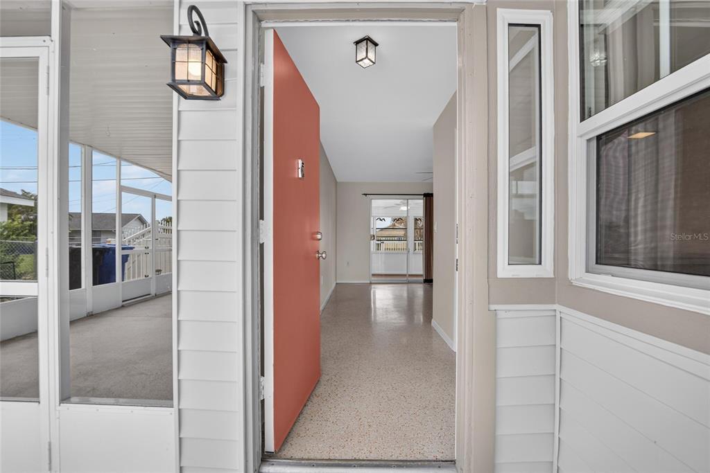 A view through an open coral-colored front door into a home with terrazzo flooring — 705 THUNDERBIRD AVENUE, SUN CITY CENTER, FL