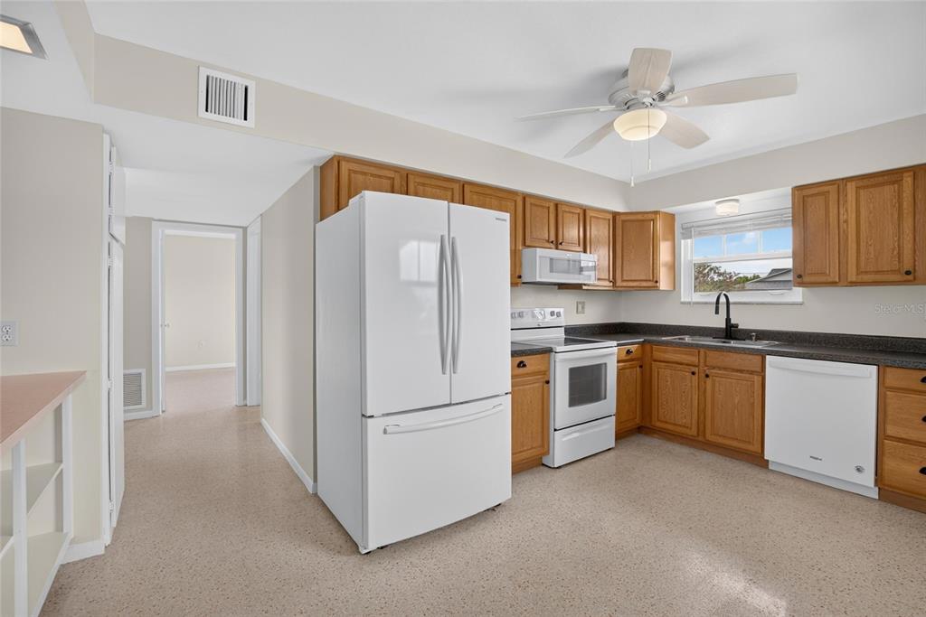 A kitchen features wood cabinets, white appliances, dark countertops, and a ceiling fan — 705 THUNDERBIRD AVENUE, SUN CITY CENTER, FL