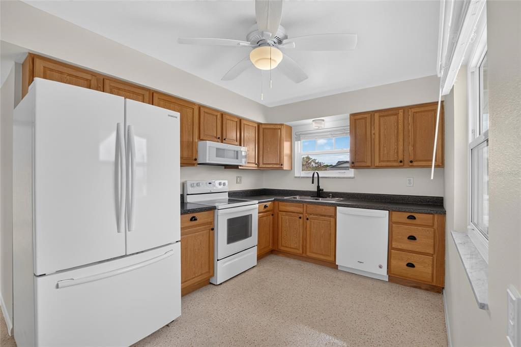 A kitchen features oak cabinets, white appliances, a dark countertop, and a ceiling fan — 705 THUNDERBIRD AVENUE, SUN CITY CENTER, FL