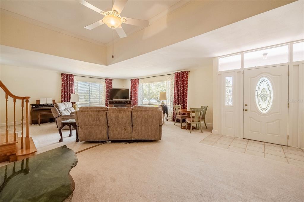 A spacious living room features a tray ceiling, beige carpeting, and a front entryway door — 102 S LAKESHORE BOULEVARD, LAKE WALES, FL