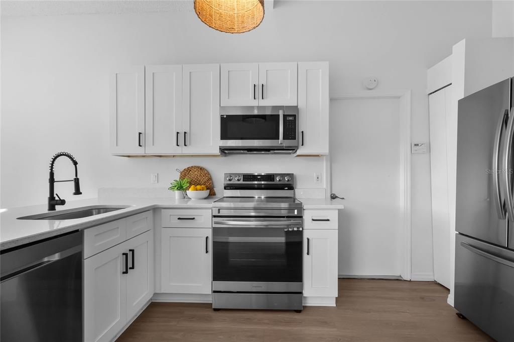 A kitchen features white cabinetry, stainless steel appliances, a dark faucet, and light wood flooring — 239 PANORAMA DRIVE, WINTER SPRINGS, FL