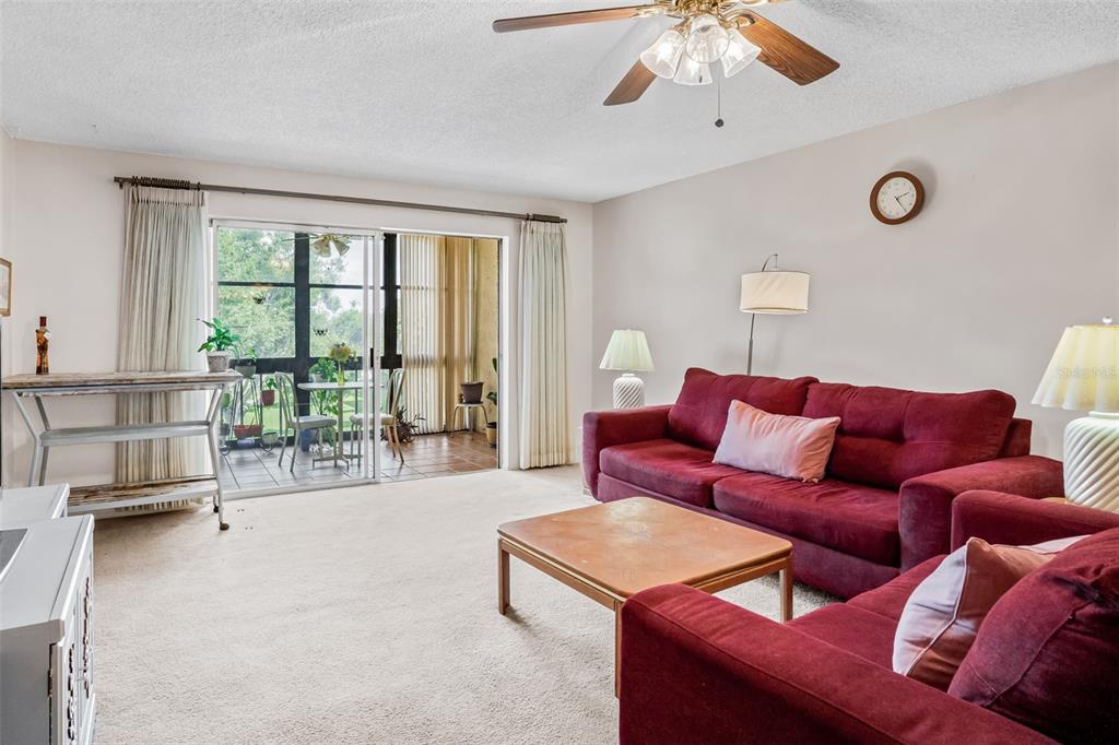 A living room features red sofas, a coffee table, and a sliding door to a patio — 11485 OAKHURST ROAD UNIT 200-306, LARGO, FL