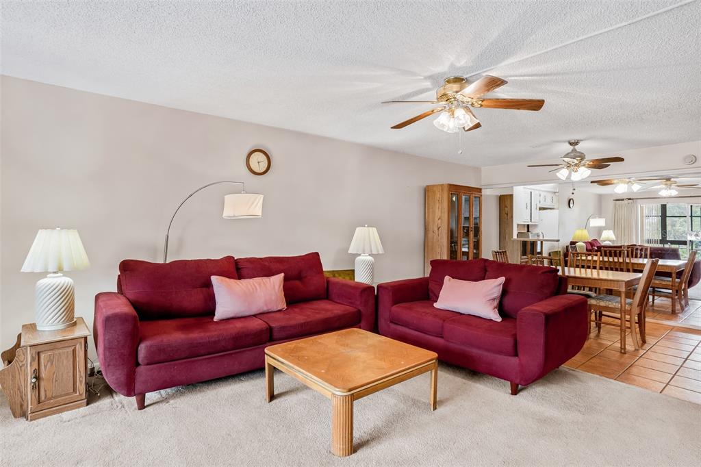 A living room features two red sofas, a wooden coffee table, and beige carpeting — 11485 OAKHURST ROAD UNIT 200-306, LARGO, FL