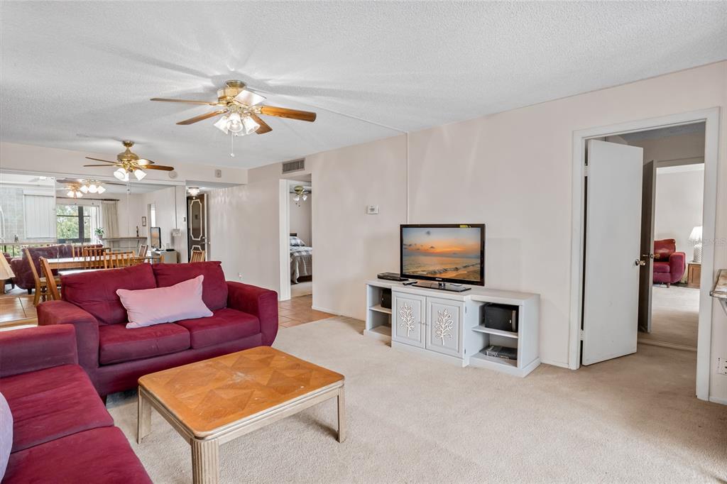 A living room features a red sofa, a wooden coffee table, and a television console — 11485 OAKHURST ROAD UNIT 200-306, LARGO, FL