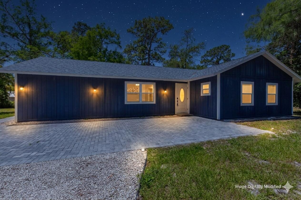 A dark blue, single-story house with a paved driveway and exterior lighting at night — 16932 W Aintree Drive W, FL 33470, FL