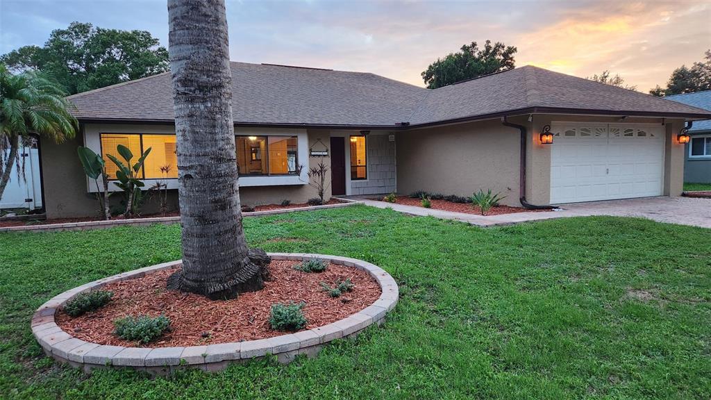 A single-story house with a tan stucco exterior, a two-car garage, and a palm tree — 15711 SCRIMSHAW DRIVE, TAMPA, FL