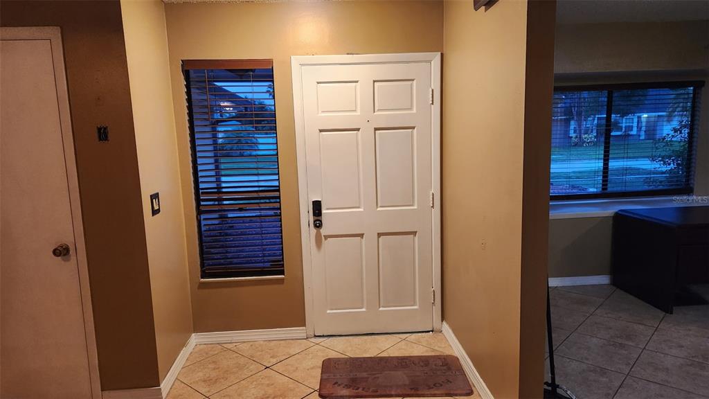 An entryway features a white front door, a side window with blinds, and tiled flooring — 15711 SCRIMSHAW DRIVE, TAMPA, FL