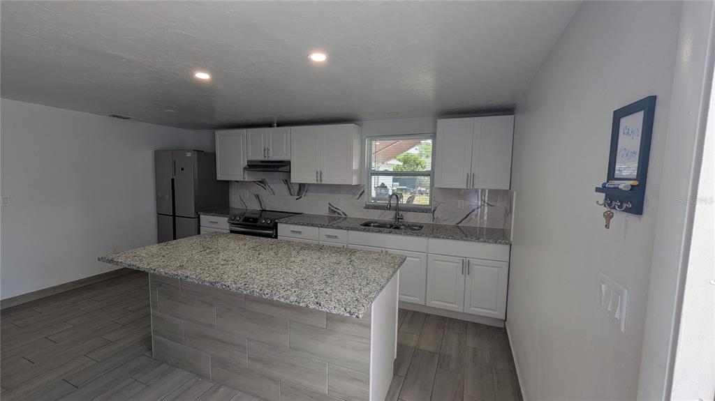 A kitchen features white cabinets, granite countertops, a matching island, and light wood-look tile flooring — 5723 9TH STREET CIRCLE E, BRADENTON, FL