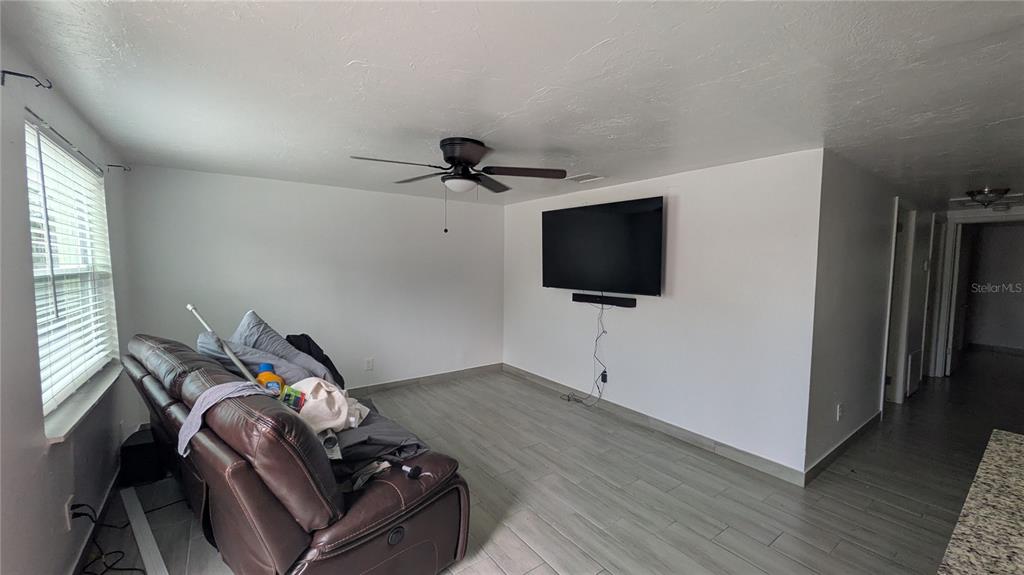 A living room features light wood-look tile flooring, a ceiling fan, and a wall-mounted television — 5723 9TH STREET CIRCLE E, BRADENTON, FL