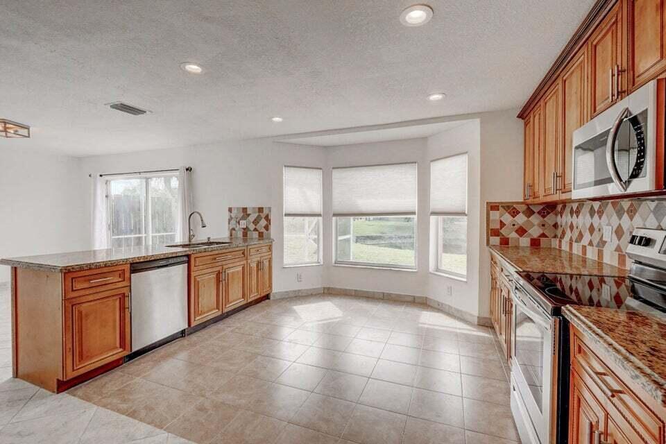 A kitchen with wood cabinets, granite countertops, tile flooring, and a bay window eating area — 10758 Lake Jasmine Drive, Boca Raton FL 33498, BOCA RATON, FL
