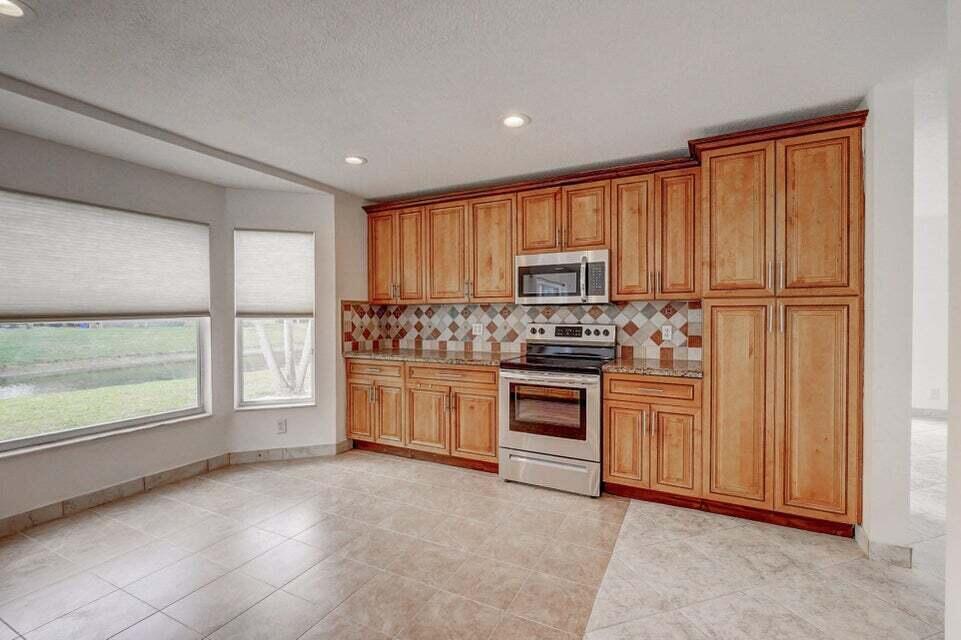 A kitchen with light wood cabinets, stainless steel appliances, and a tiled backsplash and floor — 10758 Lake Jasmine Drive, Boca Raton FL 33498, BOCA RATON, FL