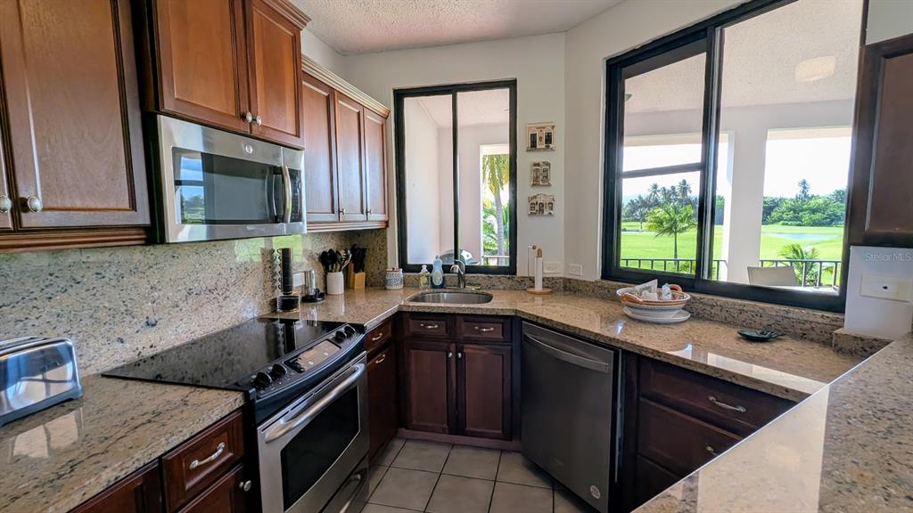 A kitchen features dark wood cabinets, granite countertops, stainless steel appliances, and a view outdoors — 185 CANDELERO DRIVE UNIT 671, HUMACAO, PR