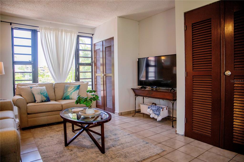 A living room with a beige sofa, glass coffee table, television, and louvered closet doors — 185 CANDELERO DRIVE UNIT 671, HUMACAO, PR