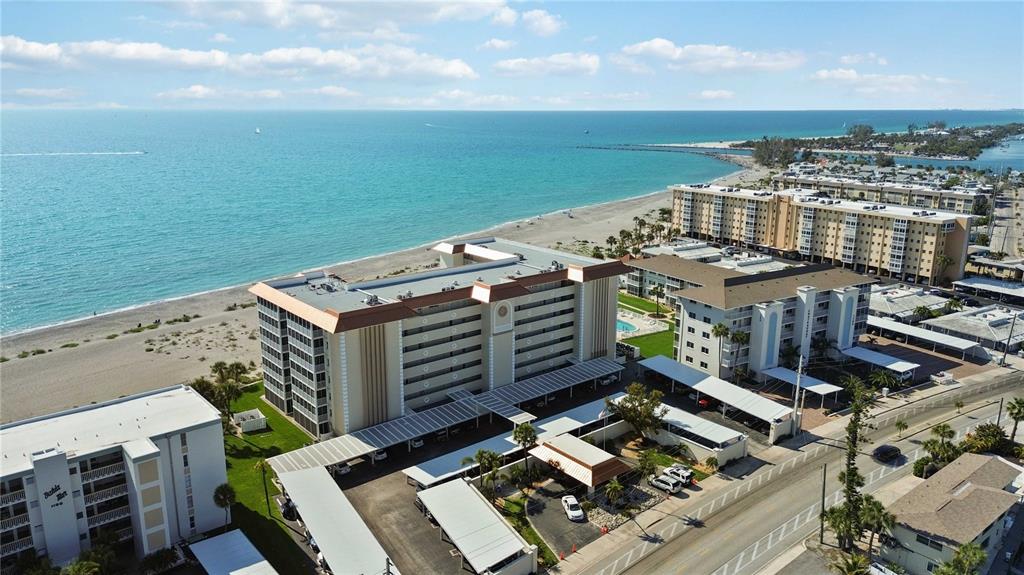 An aerial view shows beachfront condominium buildings with covered parking lots along a coastal road — 1150 TARPON CENTER DRIVE UNIT 208, VENICE, FL