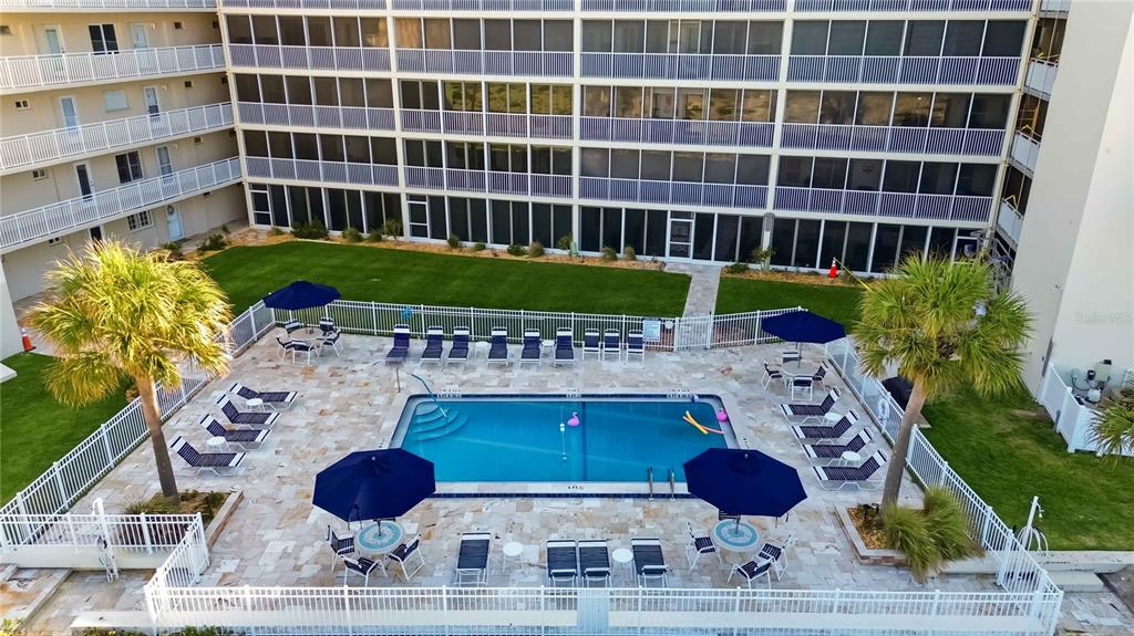 An aerial view shows a rectangular swimming pool surrounded by lounge chairs and blue umbrellas — 1150 TARPON CENTER DRIVE UNIT 208, VENICE, FL