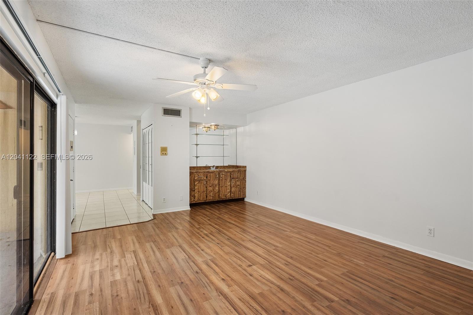 An empty room features wood-look flooring, a ceiling fan, and a built-in wet bar — 3118 Spanish Wells Dr # C, Delray Beach FL 33445, DELRAY BEACH, FL