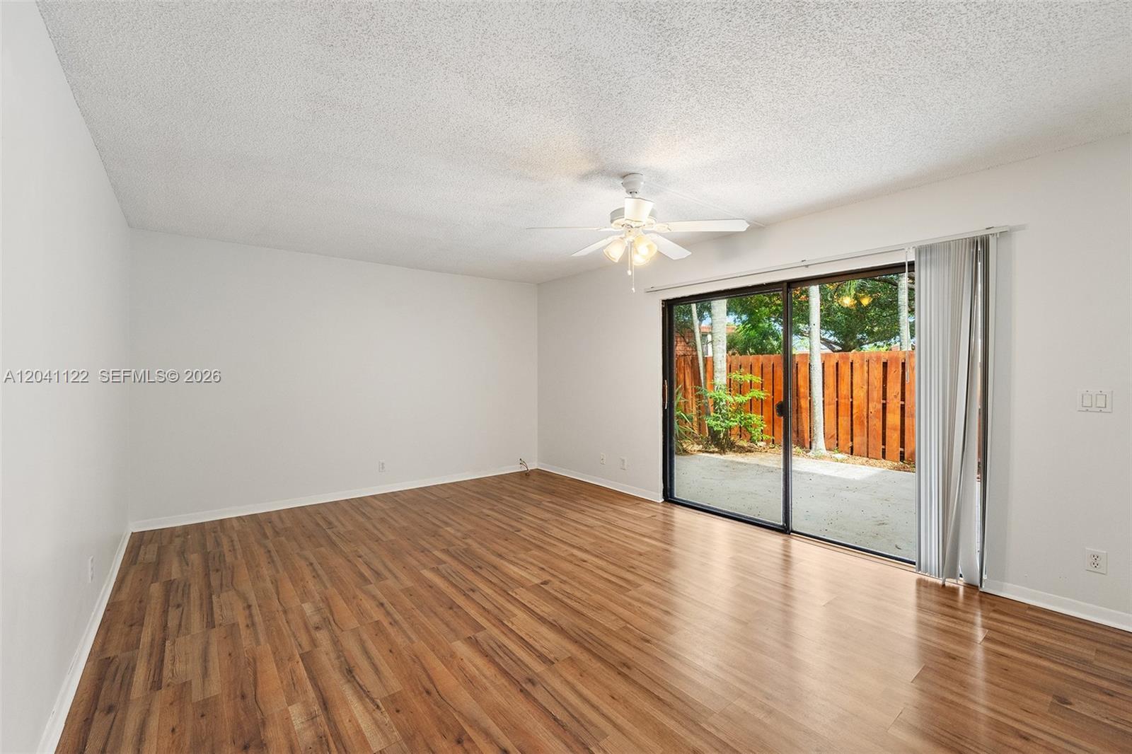 An empty room features wood-look flooring, a ceiling fan, and sliding glass doors to a patio — 3118 Spanish Wells Dr # C, Delray Beach FL 33445, DELRAY BEACH, FL