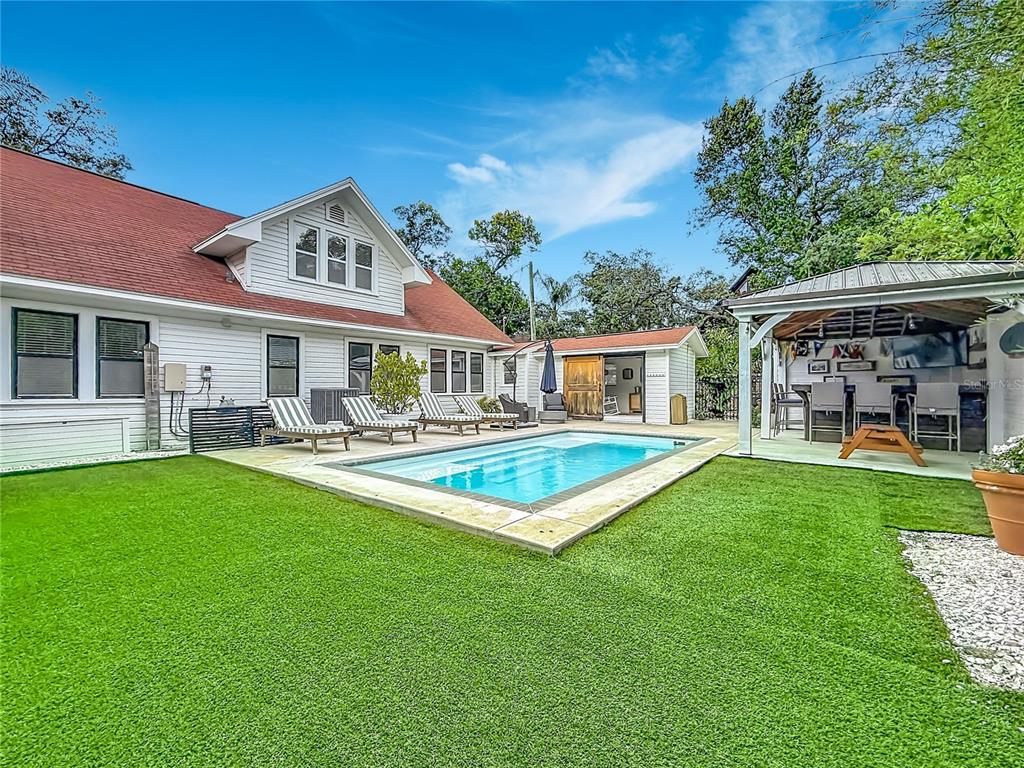 A backyard features a swimming pool, artificial turf, lounge chairs, and a covered outdoor patio — 675 S VINCENT STREET, CRYSTAL BEACH, FL