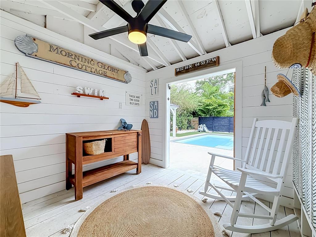 A white-walled pool house features a wooden console, rocking chair, and a view of a pool — 675 S VINCENT STREET, CRYSTAL BEACH, FL