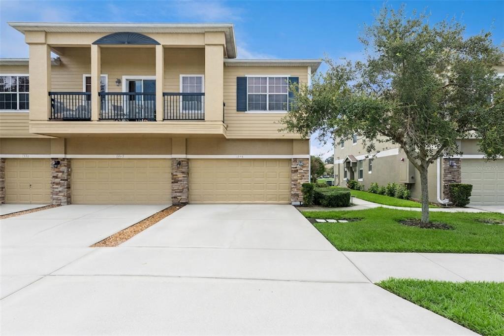 A two-story townhouse exterior features tan siding, stone accents, and a two-car garage — 1668 SCARLET OAK LOOP UNIT C, WINTER GARDEN, FL