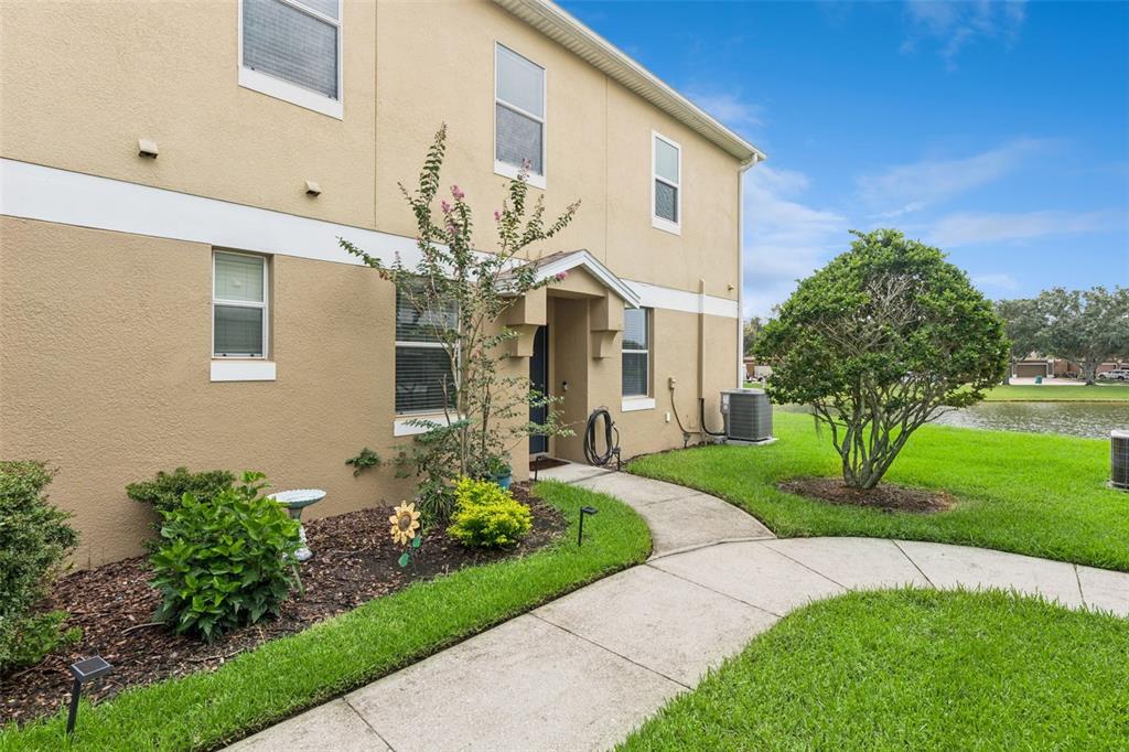 A tan two-story townhouse exterior with a concrete walkway, landscaping, and a nearby pond — 1668 SCARLET OAK LOOP UNIT C, WINTER GARDEN, FL