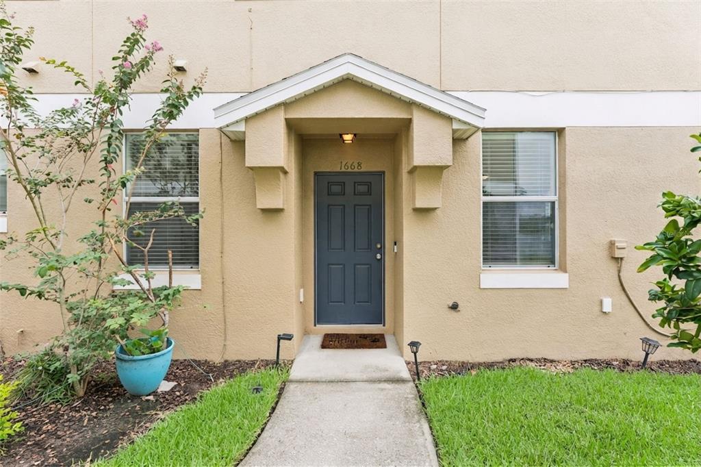 A tan stucco building exterior features a covered entryway with a dark gray front door — 1668 SCARLET OAK LOOP UNIT C, WINTER GARDEN, FL