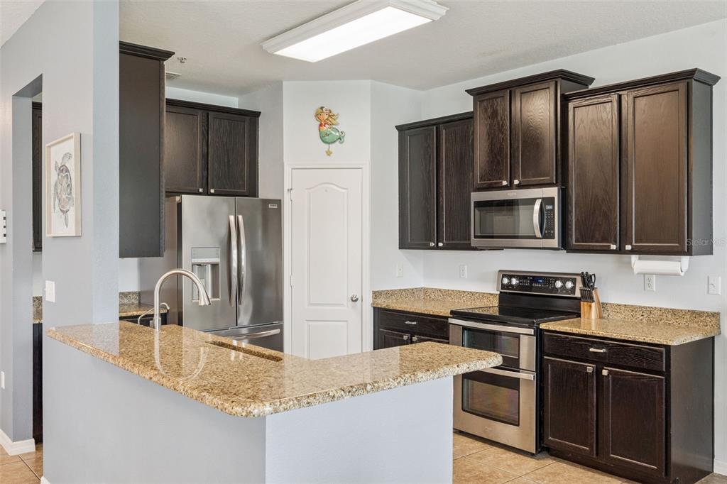 A kitchen features dark wood cabinets, granite countertops, and stainless steel appliances — 1668 SCARLET OAK LOOP UNIT C, WINTER GARDEN, FL