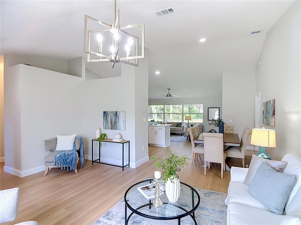 An open-concept living and dining area features light wood flooring and a modern metal chandelier — 6353 FORESTWOOD DRIVE E, LAKELAND, FL