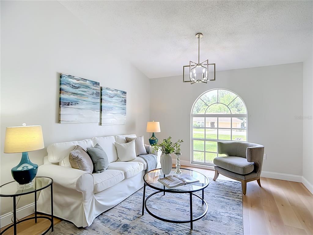 A living room features a white sofa, a glass coffee table, and an arched window — 6353 FORESTWOOD DRIVE E, LAKELAND, FL