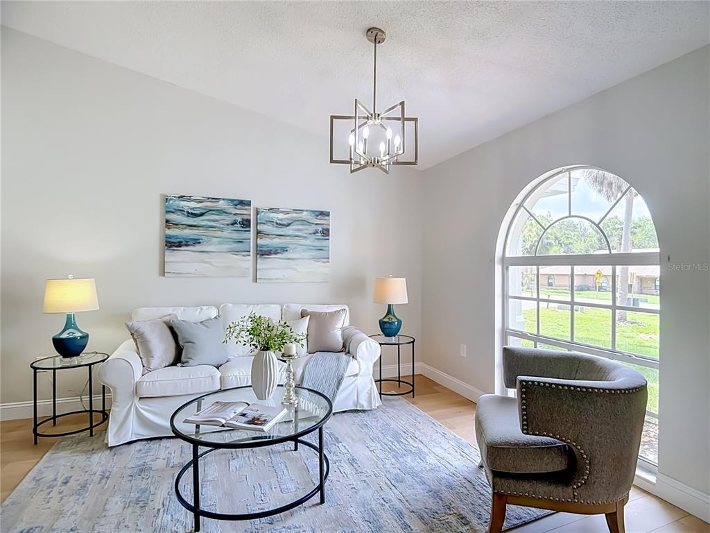 A living room features a white sofa, a gray armchair, and a large arched window — 6353 FORESTWOOD DRIVE E, LAKELAND, FL