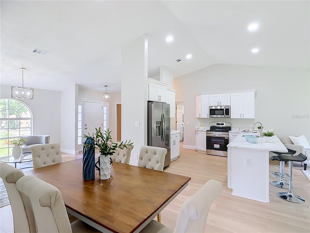 An open-concept dining area and kitchen feature white cabinetry, stainless steel appliances, and wood flooring — 6353 FORESTWOOD DRIVE E, LAKELAND, FL