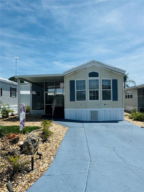 A light-colored manufactured home features a covered porch, blue shutters, and a paved driveway — 300 ROYAL TROON LOOP, DAVENPORT, FL