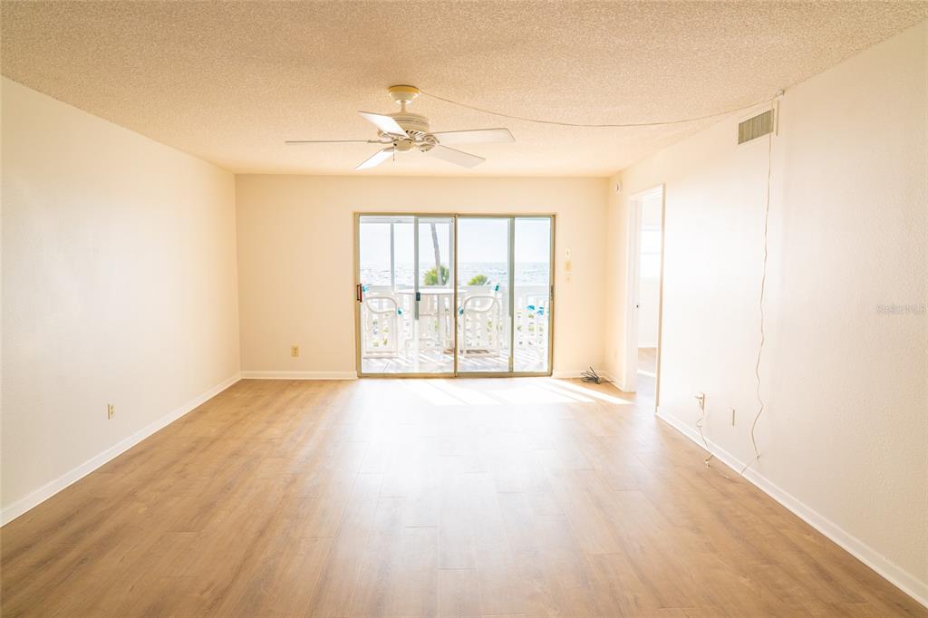 An empty living room with light wood-look flooring, a ceiling fan, and sliding glass doors — 403 GULF WAY UNIT 304, ST PETE BEACH, FL