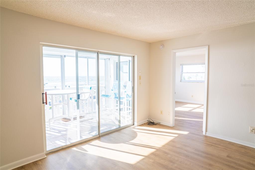 A room with light wood-look flooring, sliding glass doors to a balcony, and an adjacent room — 403 GULF WAY UNIT 304, ST PETE BEACH, FL