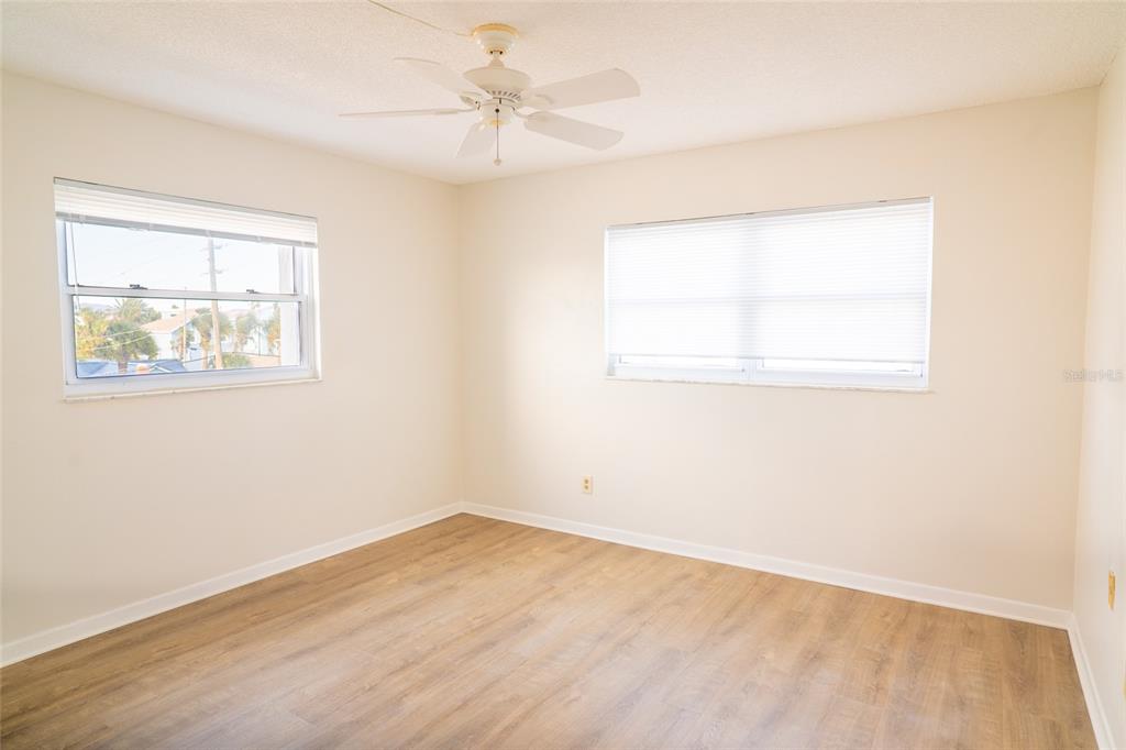 An empty bedroom features light-colored walls, wood-look flooring, a ceiling fan, and two windows — 403 GULF WAY UNIT 304, ST PETE BEACH, FL
